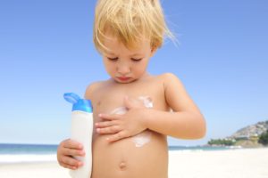 summer vacation: cute child applying sunscreen at the beach